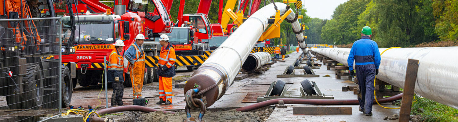 Bouwvakkers bezig met het installeren van grote pijpleidingen op een bouwplaats van WarmtelinQ.
