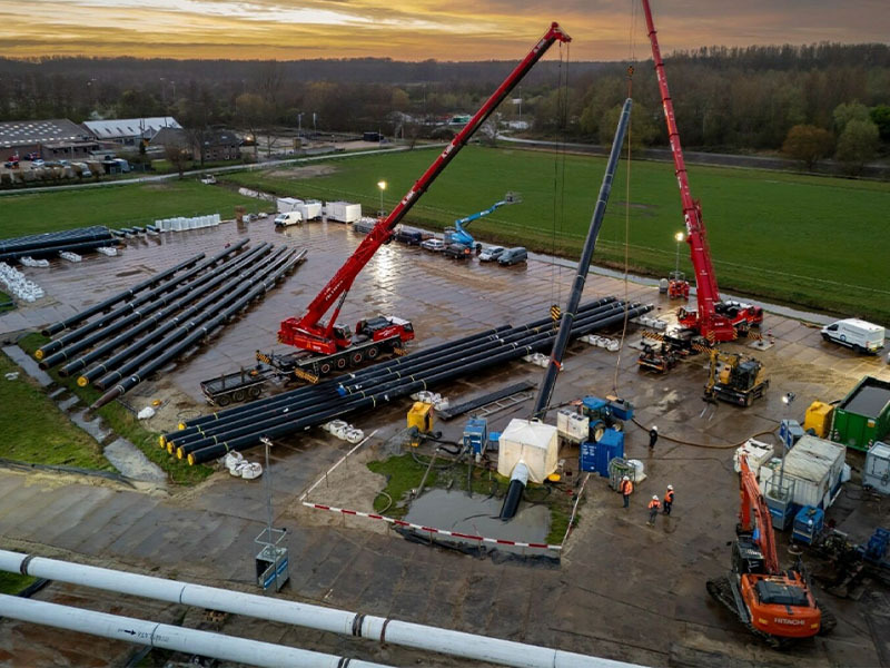 Bouwplaats van WarmtelinQ bij zonsondergang met kranen en pijpleidingen.